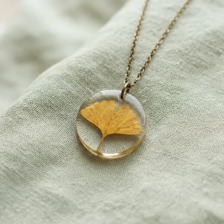 Runder Anhänger aus Epoxidharz mit goldenem Ginkgoblatt an einer feinen Messingkette